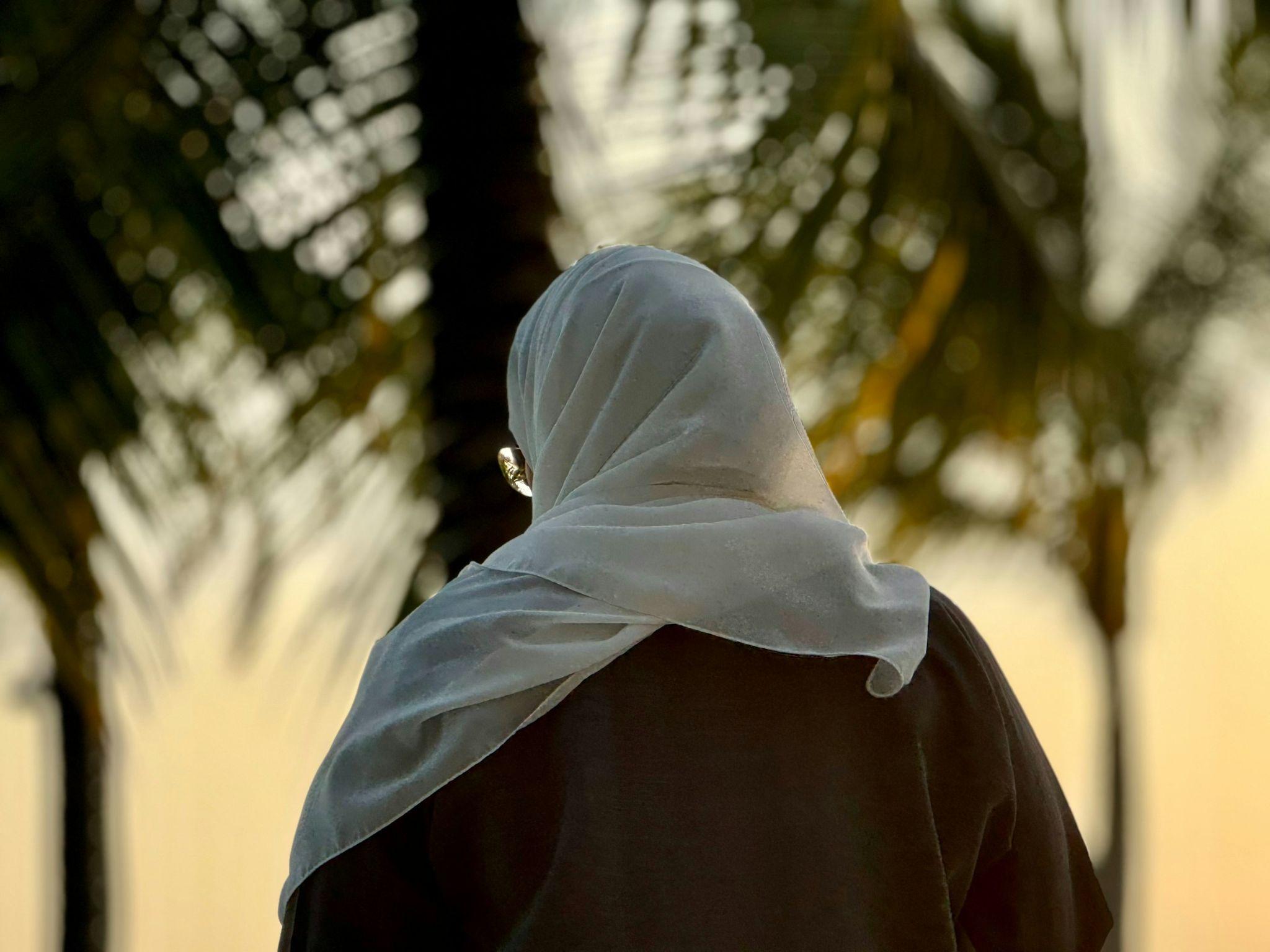 Femme musulmane en hijab vue de dos marchant près d'un palmier en Arabie Saoudite