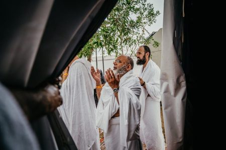Pilgrims in ihram raising their hands in supplication during Umrah in Makkah