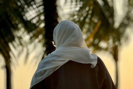 Veiled woman from behind near a palm tree